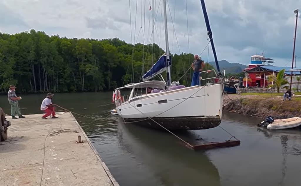 White sailboat secured at concrete boatyard dock in river estuary with crew handling mooring lines before haul-out